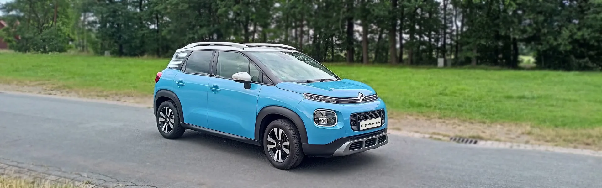 Ki-gesteuerter Citroen C3 Aircross #3 Bild 3: Ki-gesteuerter hellblauer Citroen C3 Aircross mit weißem Dach fährt auf einer Strasse vor Bäumen